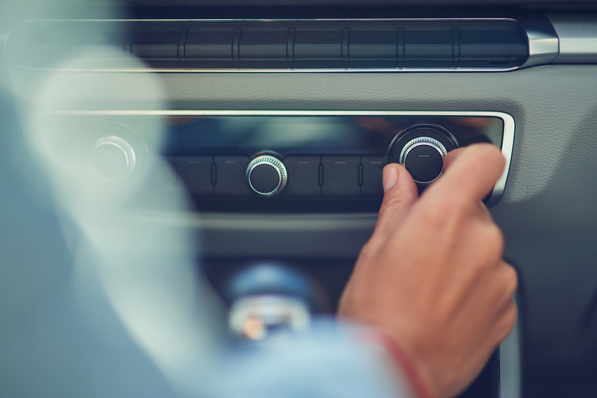 A car radio is shown. A person is turning the volume control.